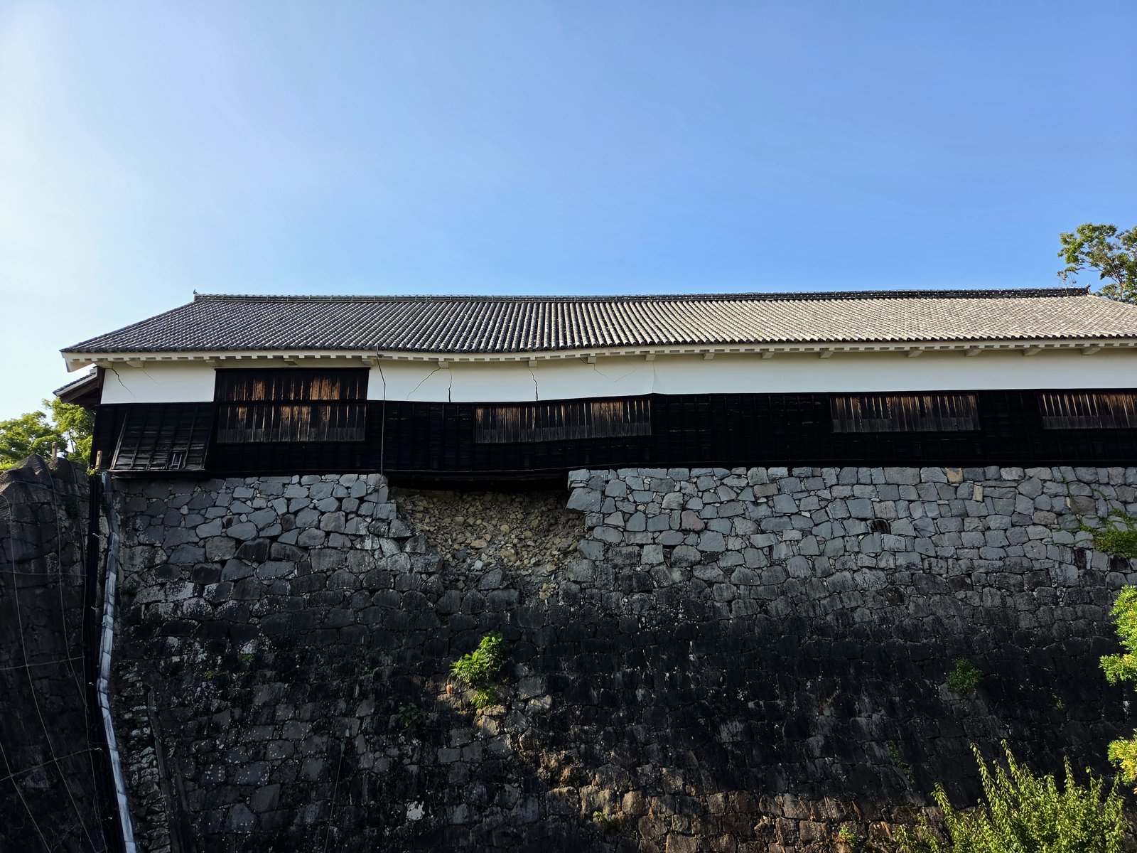 Muralha de pedra e torre de madeira do Castelo de Kumamoto, com trechos de pedras faltando e rachaduras