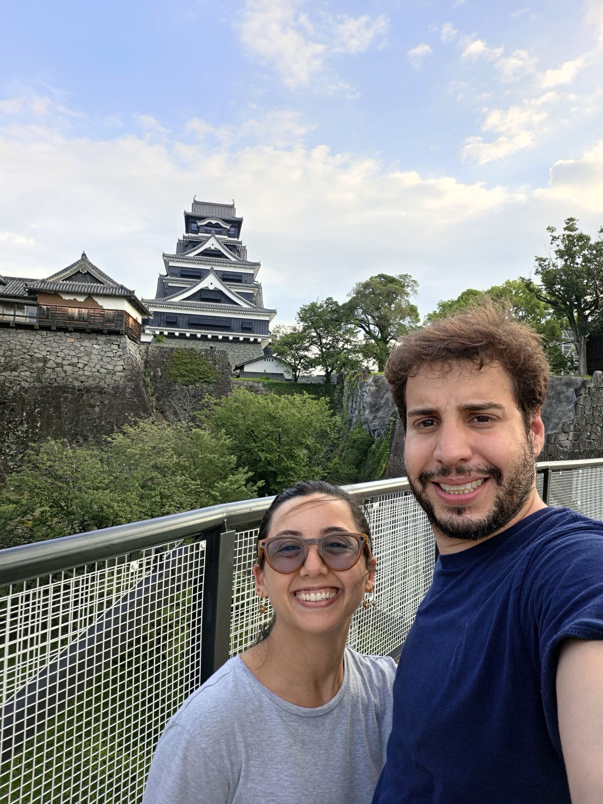 Selfie da Rapha e do Adam na passarela elevada, com o Castelo de Kumamoto ao fundo